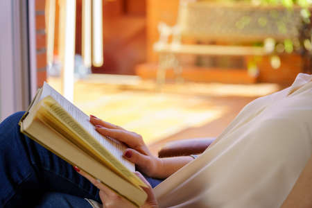 White woman reading a book in an armchair relaxing in nice daylight outside. Copy space. Reading,...