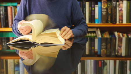 white man reading book at a glass table and bookstore background with lots of books. Copyspace....