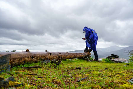 Man looking at the mobile at the top of the mountain on a rainy day.
