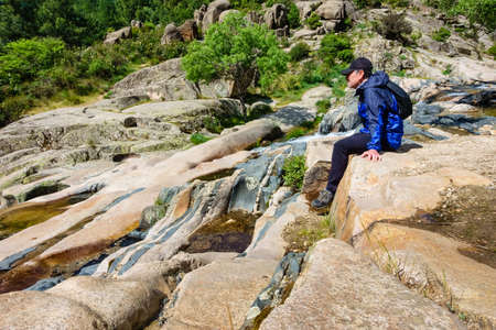 Rocky landscape with waterfalls and man sitting on a rock resting.