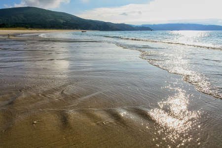 Deserted beach with gentle waves on the sand and reflection of the sun in the water.の写真素材