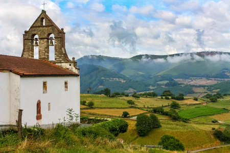 Ancient church with bell tower in the green field with high mountains in the background. AsturiasSpainEurope.の写真素材