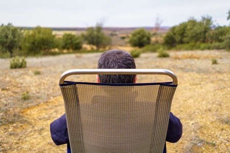 Man from the back sitting in a camping chair, enjoying the countryside.