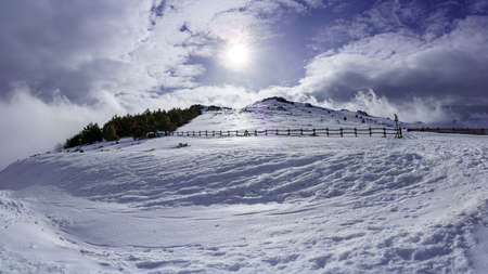 High mountain snowy landscape with sun rays and sky with clouds.