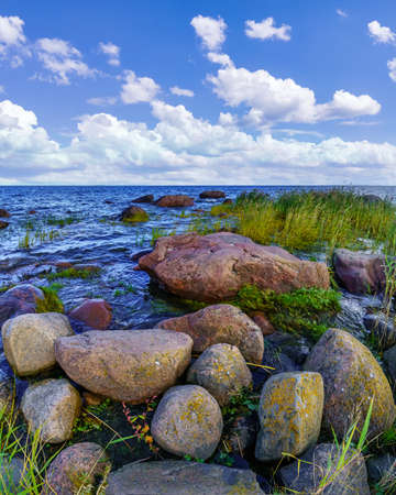 Seascape with large rocks on the shore and white clouds over blue sky.の写真素材