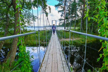 Woman passing over a wooden bridge and steel cables over the calm river.の写真素材
