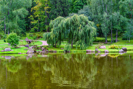 Japanese garden with lush trees that are reflected in the calm water of the river.の写真素材