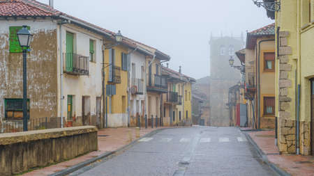 Alley of old houses with a church in the background on a day with thick fog and mystical atmosphere. Riaza Segovia.の写真素材