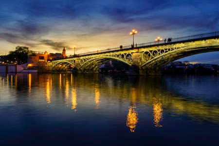 Triana bridge in Seville over the Guadalquivir river at sunset, with lights reflecting in the river water, an idyllic and charming scene. Andalusia.の写真素材