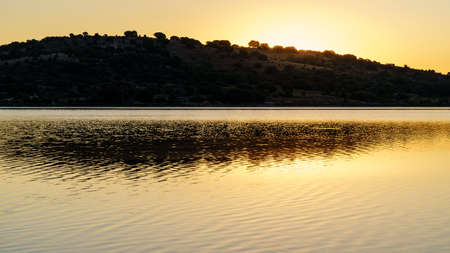 Landscape at sunrise with golden light and reflections of the mountain in the lake water. Spain.の写真素材