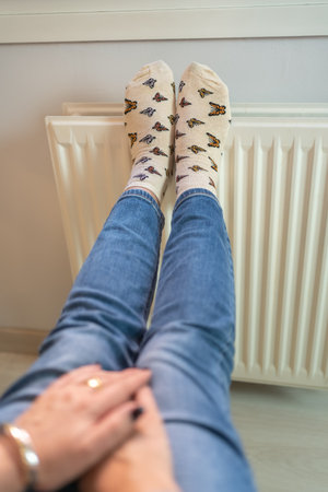 Woman with her feet resting on a radiator to warm them up due to the cold of winter.