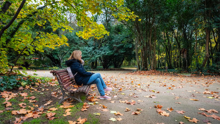 Woman sitting on a wooden bench in public park on a cold winter day.の写真素材