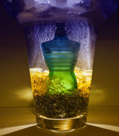 Perfume bottle, inside a jar with pebbles yellow, with water falling from above, behind illuminated in yellow background のeditorial素材