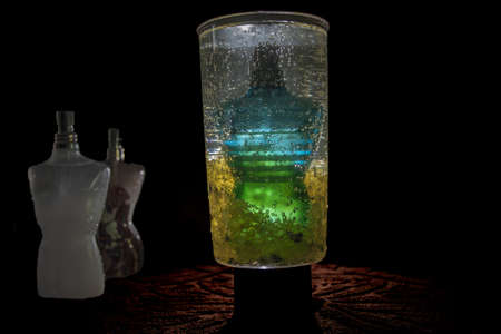 Perfume bottle, inside a cup with pellets and pebbles yellow illuminated behind, with two adjacent bottles prefumeのeditorial素材