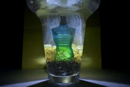 Perfume bottle, inside a jar with pebbles yellow, with water falling from above, behind illuminated in yellow background のeditorial素材