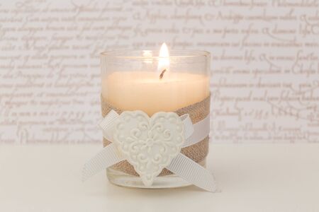 Glass with lit candle and white heartの写真素材
