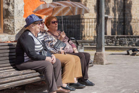 Potes, Cantabria, Spain; 18 03 2017: 3 elderly women smiling with hat, sunglasses and an umbrella sitting on a benchのeditorial素材