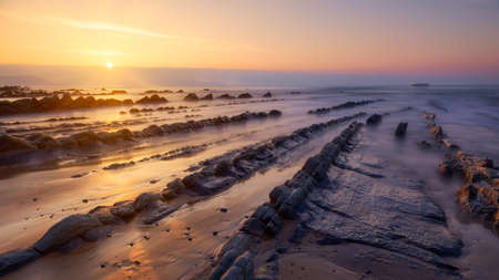 Warm sunset at Barrika beach with several rows of rocks directing the gaze towards an oil tanker. 16:9 ratio.の写真素材
