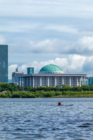 SEOUL, SOUTH KOREA - MAY 5, 2018: The National Assembly in Seoul, South Korea with a kayak paddling by on the Han river. Taken from Hapjeong Han-river park.のeditorial素材