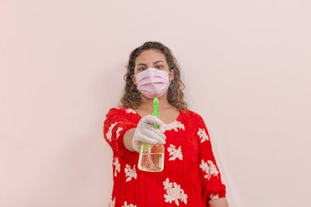 Latin woman taking precautions by covid-19 wear a face mask, gloves and sprayer to prevent infectionの写真素材