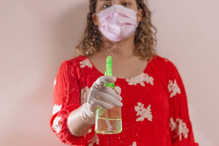 Latin woman taking precautions by covid-19 wear a face mask, gloves and sprayer to prevent infectionの写真素材