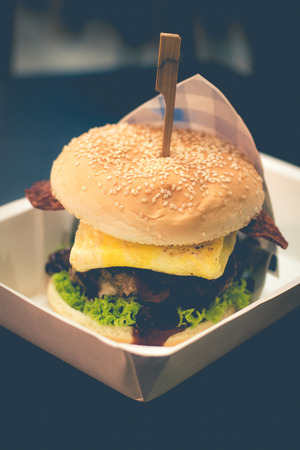 Homemade chicken or beef patty, fried egg, crispy turkey bacon, cheese, lettuce, tomato, cucumberの写真素材