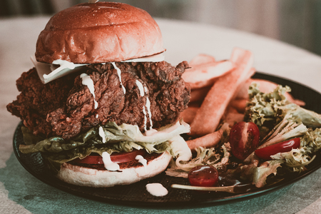 Grilled brioche burger with chef creation fried chicken, lettuce, tomatoes, monterey cheese, mixed salad with olive oil vinagrette and french friesの写真素材