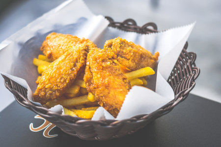 crispy golden brown fried chicken wings served in a basket with friesの写真素材