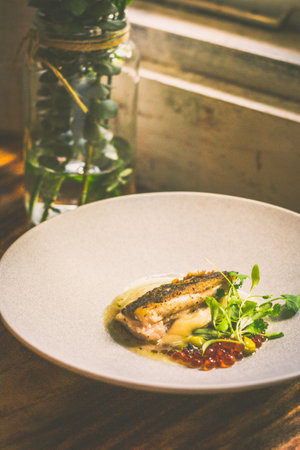 Threadfin with yucca mash, fermented tomato fish jus, laksa oil, pickled fava beans, ikura, capersの写真素材