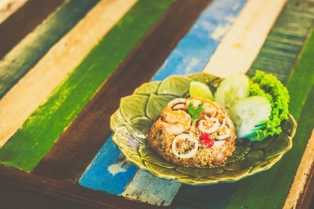 Tom Yum Seafood Fried rice served with cucumber and lettuce on the sideの写真素材