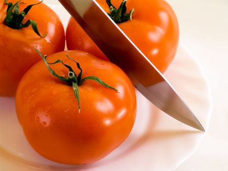 Three tomatos and knife on the plate.