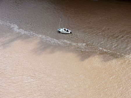 Small motorboat sailing up on a dirt filled river.の写真素材