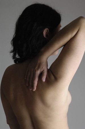 Nude woman with back pain on a gray backgroundの写真素材