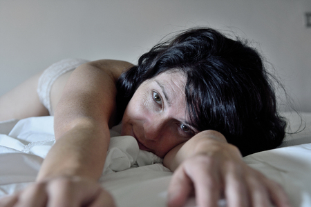 nude woman looking at camera lying on the bedの写真素材