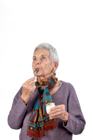 senior woman eating yogurt on white backgroundの写真素材