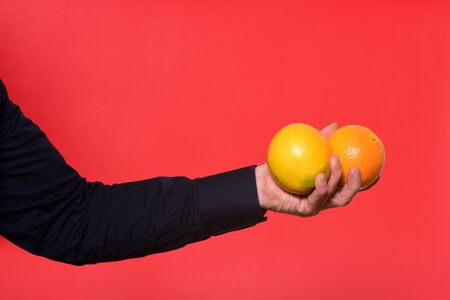 hand holding two orange fruit on red backgroundの写真素材