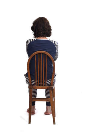 rear view of a woman in pajamas sitting o a chair on white backgraund, arms crossedの写真素材