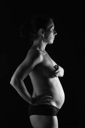 portrait of pregnant woman naked sideways on black background, six months; black and whiteの写真素材