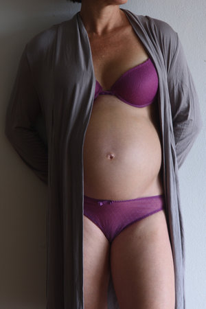 detail of the belly of a pregnant woman leaning on the wallの写真素材
