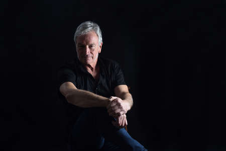 front view portrait of senior man sitting on chair on black background