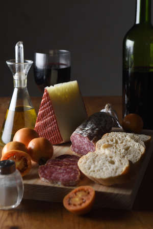 view of a typical spanish food, tomato, wine, bread, cheese, sausage and olive oil on a wooden table