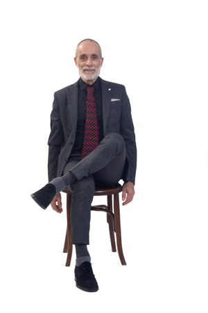 front view of a man sitting on chair with suit and tie and cross legged and arms crossed looking at camera on white backgroundの写真素材
