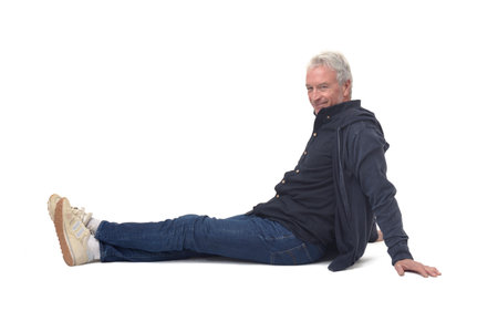side view of a man sitting on the floor with his legs stretched and looking at camera out on white backgroundの写真素材