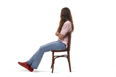 Side view of a young girl sitting on chair with arms crossed look at the bottom on white backgroundの写真素材