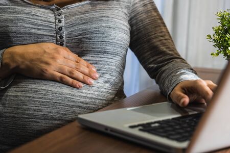Pregnant white woman working with a laptop on a wood tableの写真素材