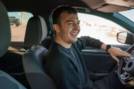 Man inside the car sitting in the driver's seat, smiling with one arm resting on the window. Caucasian, dark hair and stubble. He is wearing a smart watch while holding the handlebars.の写真素材