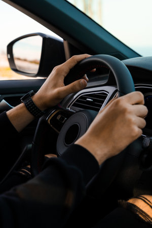 Close-up of hands holding the handlebars of a car, wearing a smart watch on the wrist. Wearing dark,...