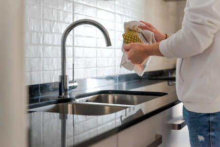 Unrecognizable man in the kitchen. He is drying the dishes. In a white kitchen with black marble. There is natural light inside in Spain.の写真素材