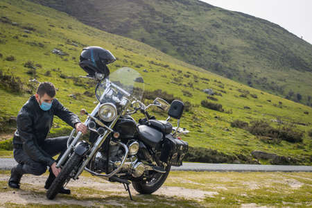 Young handsome biker checking his custom motorcycle while wearing a facial maskの写真素材