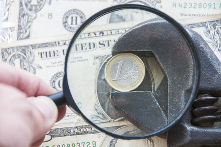 spanner with euro on background of a dollar with magnifying glassの写真素材